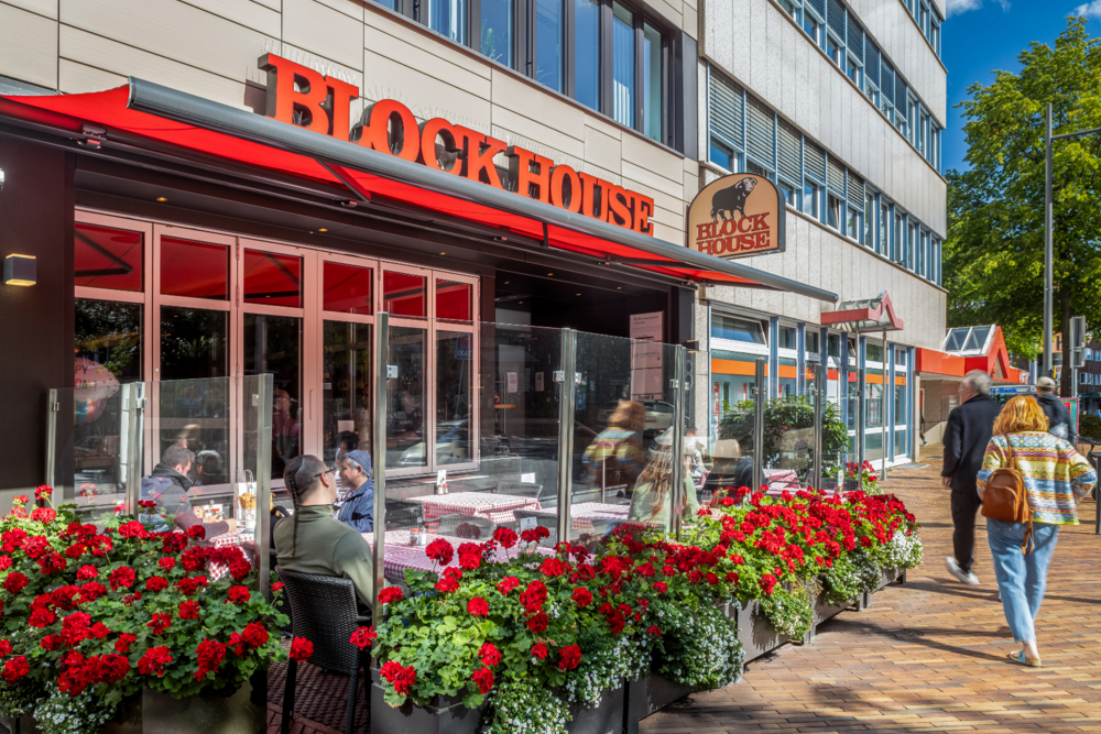 BLOCK HOUSE Hamburg Harburg – Steakhouse mit Außenterrasse Terrasse des BLOCK HOUSE Hamburg Harburg mit Gästen und rotem Logo auf der Gebäudefassade