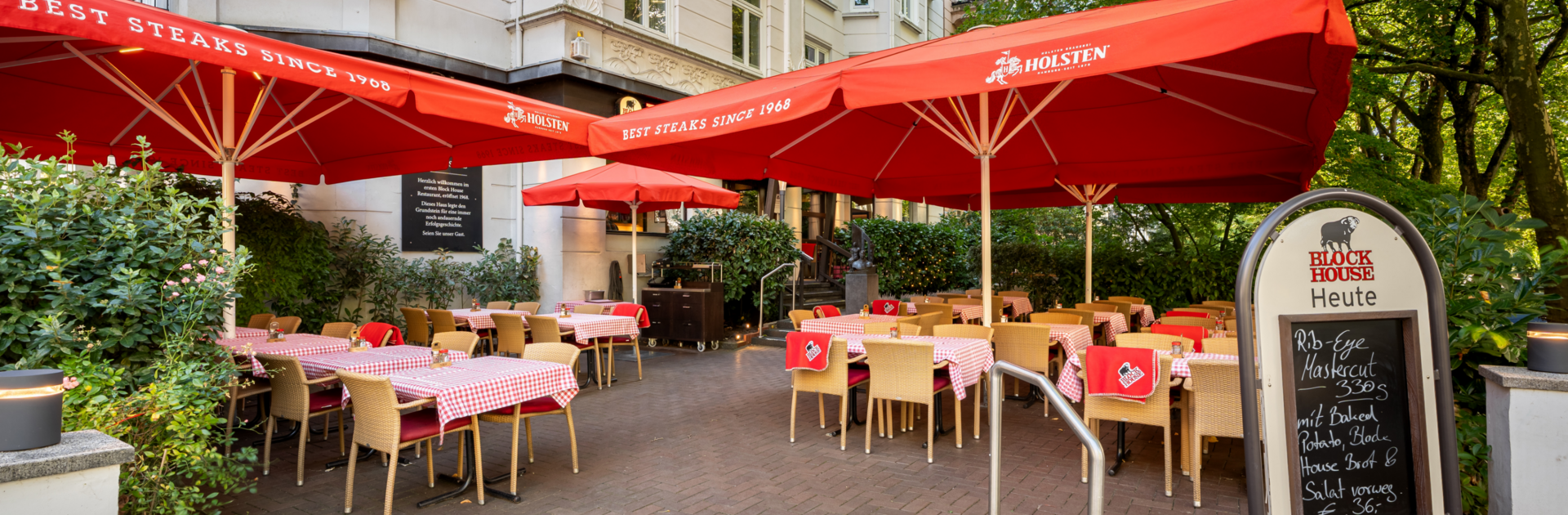 BLOCK HOUSE Hamburg Winterhude – Erstes Steakhouse seit 1968 Eingangsbereich und Terrasse des BLOCK HOUSE Hamburg Winterhude mit Sonnenschirmen, Sitzplätzen und altem Baumbestand