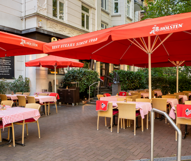 BLOCK HOUSE Hamburg Winterhude – Erstes Steakhouse seit 1968 Eingangsbereich und Terrasse des BLOCK HOUSE Hamburg Winterhude mit Sonnenschirmen, Sitzplätzen und altem Baumbestand