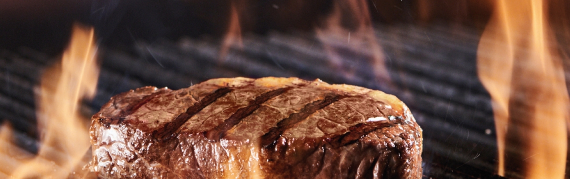 Ein Steak liegt auf einem Grill, umgeben von Flammen