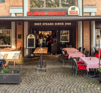 BLOCK HOUSE Ahrensburg – Steakhouse mit Terrasse Terrasse des BLOCK HOUSE Ahrensburg mit Gästen an Tischen mit rot-weiß karierten Tischdecken vor dem Steakhouse