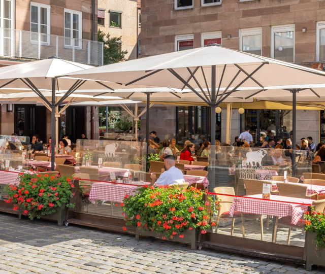 BLOCK HOUSE Nürnberg – Außenterrasse mit blühenden Geranien Speisende Gäste auf der sonnengeschützten Terrasse des BLOCK HOUSE Restaurants in Nürnberg