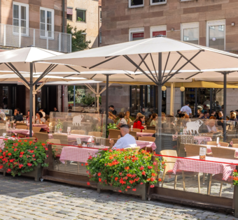 BLOCK HOUSE Nürnberg – Außenterrasse mit blühenden Geranien Speisende Gäste auf der sonnengeschützten Terrasse des BLOCK HOUSE Restaurants in Nürnberg