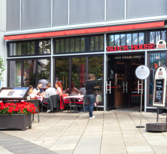 BLOCK HOUSE Stuttgart Königstraße Außenansicht des BLOCK HOUSE Stuttgart Königstraße mit Terrasse und Gästen vor dem Restaurant.