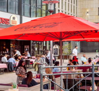 BLOCK HOUSE Essen Außenansicht des BLOCK HOUSE Essen mit großer Terrasse, roten Sonnenschirmen und Gästen im Außenbereich.