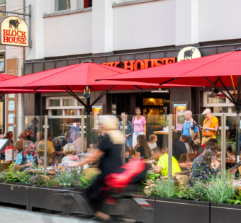 BLOCK HOUSE Hannover Am Kröpcke – Steakhouse mit Terrasse Terrasse des BLOCK HOUSE Hannover Am Kröpcke mit Gästen unter roten Sonnenschirmen in der Fußgängerzone der Innenstadt