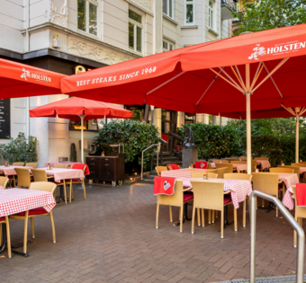 BLOCK HOUSE Hamburg Winterhude – Erstes Steakhouse seit 1968 Eingangsbereich und Terrasse des BLOCK HOUSE Hamburg Winterhude mit Sonnenschirmen, Sitzplätzen und altem Baumbestand