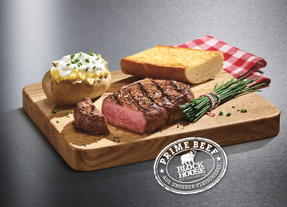 BLOCK HOUSE Prime Time Steak Ein gegrilltes, zartrosa Rumpsteak vom BLOCK HOUSE Rind, serviert auf einem Holzbrett mit einer original Baked Potato und ofenfrischem Block House Brot.
