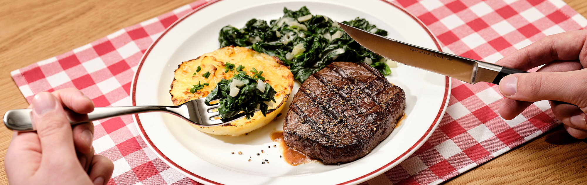 BLOCK HOUSE Lunch Time – Steak mit Kartoffelgratin und Spinat Saftig gegrilltes Rindersteak, serviert mit cremigem Kartoffelgratin und frischem Blattspinat auf einem Teller, platziert auf einer rot-weiß karierten Tischdecke.