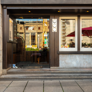 BLOCK HOUSE Stuttgart Arnulf-Klett-Platz – Steakhouse mit Terrasse Eingang des BLOCK HOUSE Stuttgart Arnulf-Klett-Platz mit Menütafel vor dem Steakhouse und Gästen an Tischen mit rot-weiß karierten Tischdecken