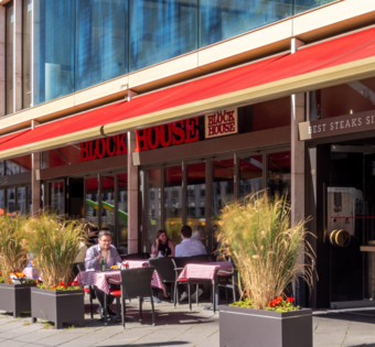 BLOCK HOUSE Frankfurt Europa-Allee – Steakhouse mit Terrasse Außenansicht des BLOCK HOUSE Frankfurt Europa-Allee mit ausgefahrener Markise und Gästen auf der Terrasse bei gutem Wetter